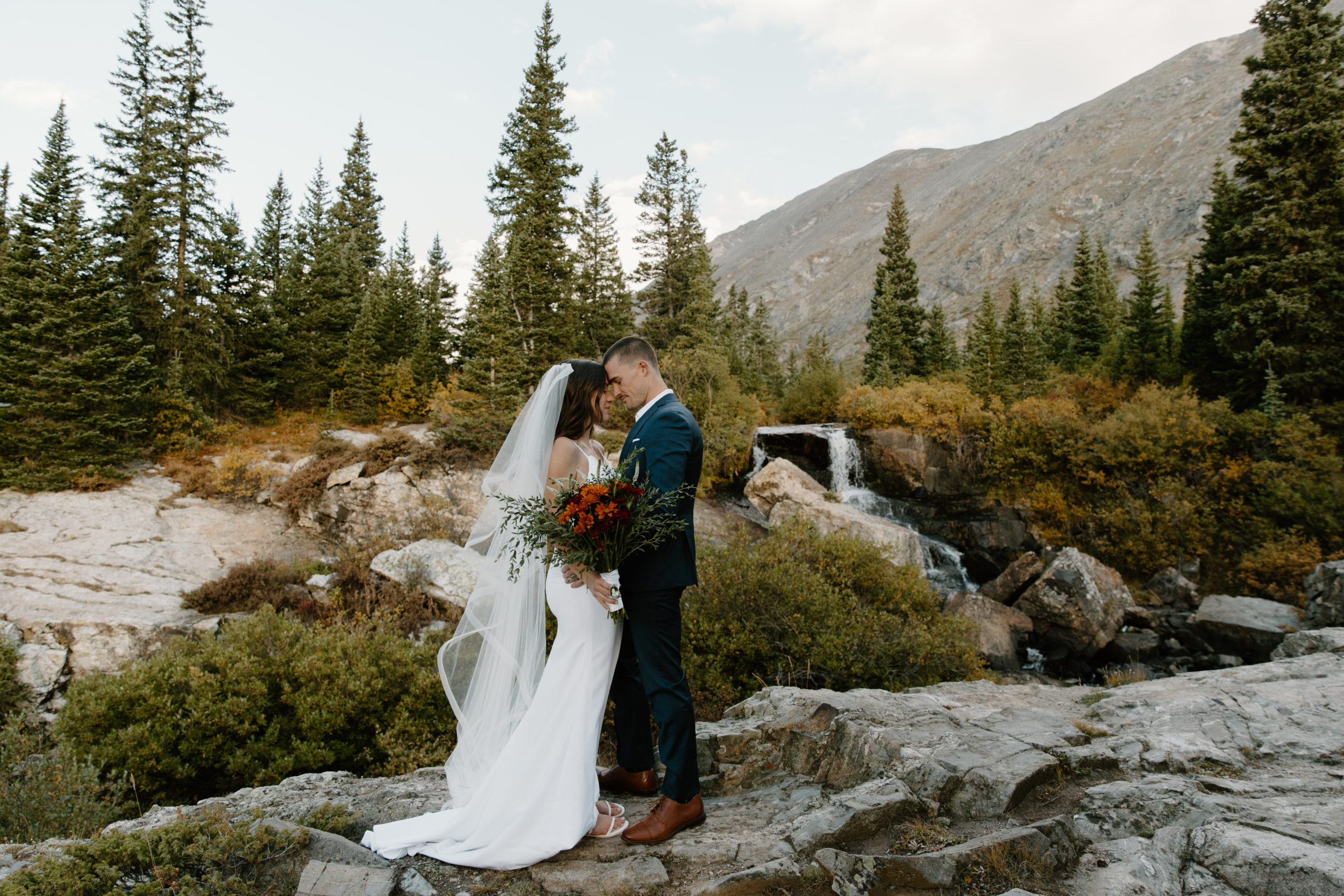 A bride and groom share their first kiss in front of a waterfall in Breckenridge, Colorado.