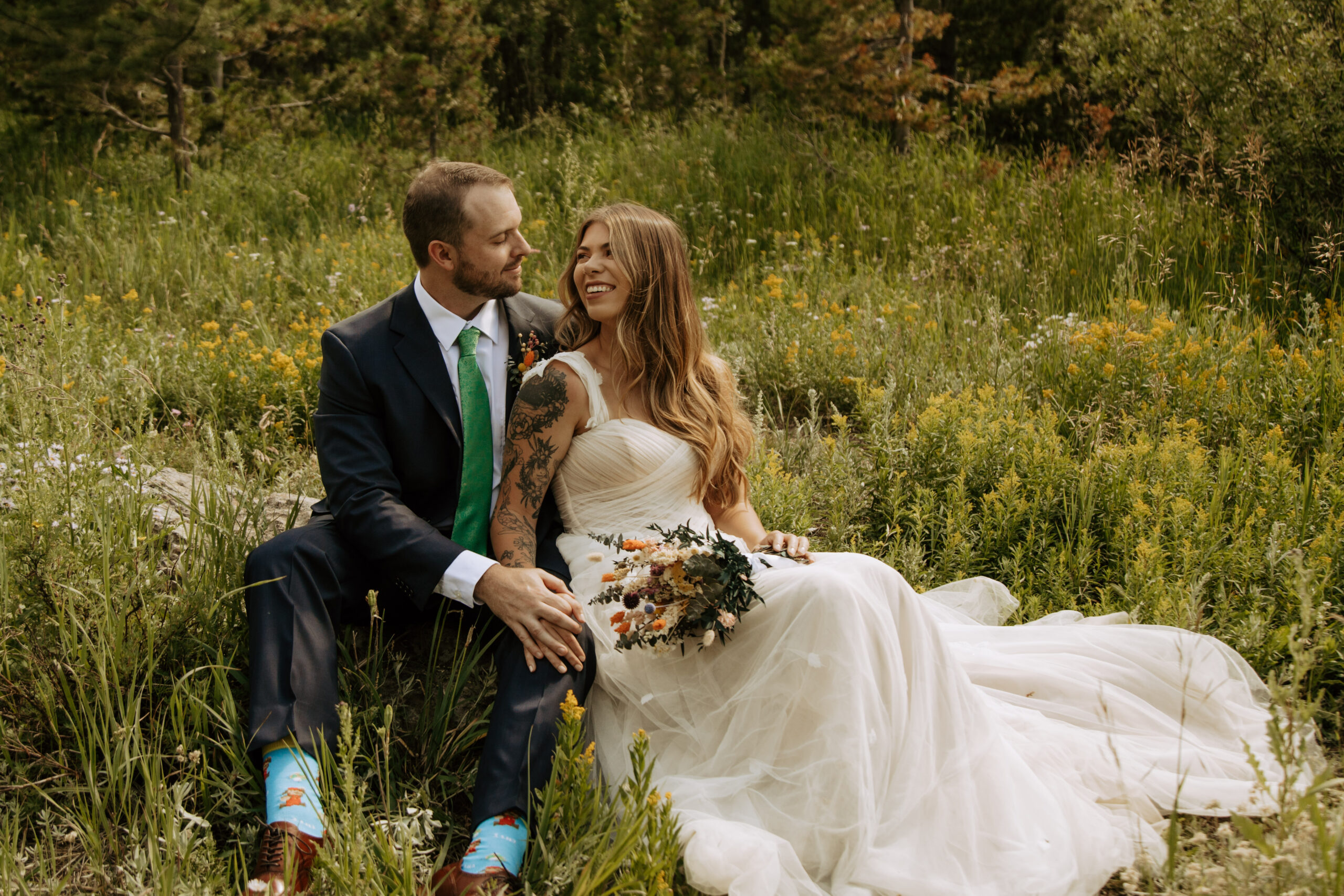 Whitney and Aaron, a bride and groom, share a happy glance as they lay in a field of wildflowers on their wedding day.