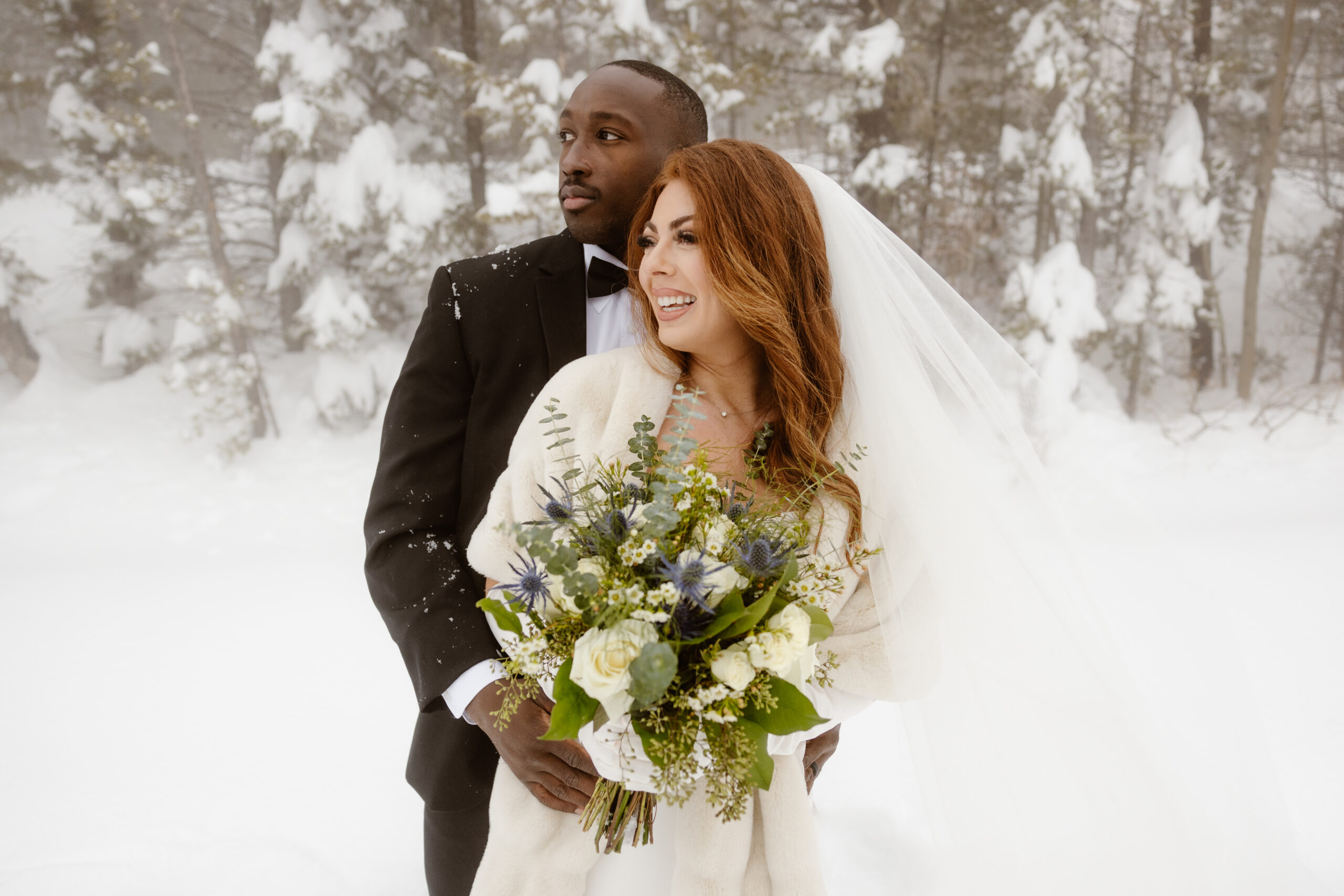 A bride and groom smiling and embracing on their snowy wedding day in Rocky Mountain National Park. 