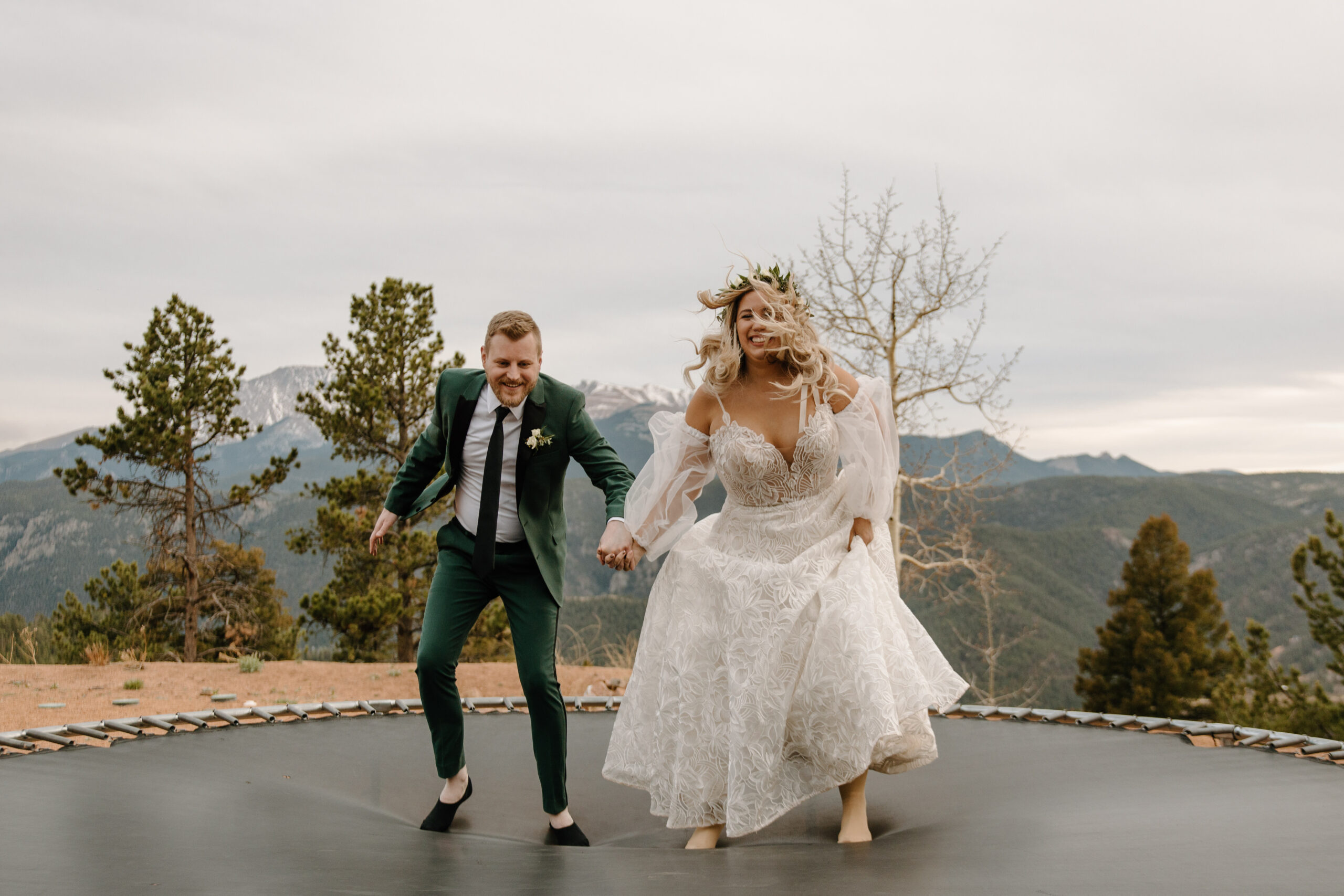Bride and groom jump on a trampoline in wedding attire after their ceremony in Colorado.