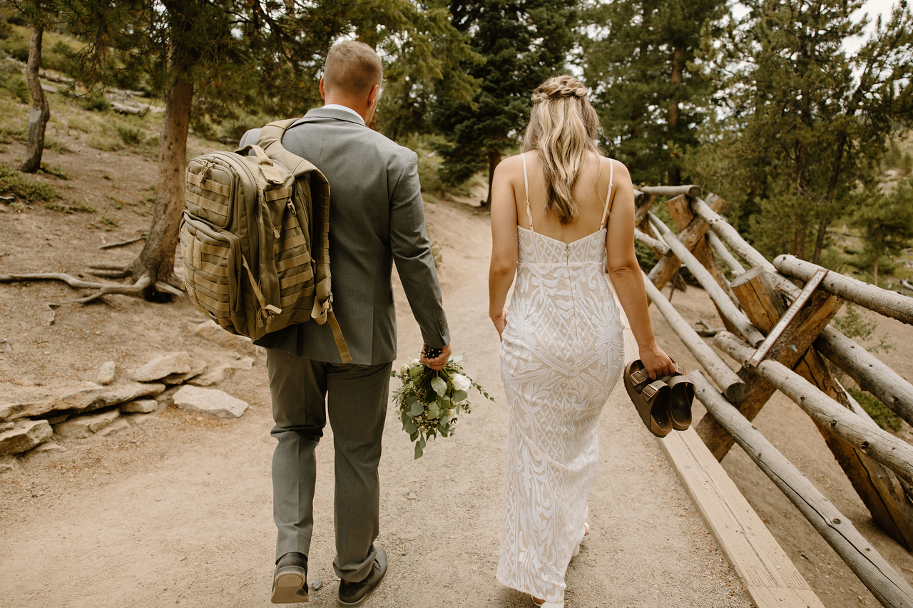 Eloping couple hikes a Colorado trail with backpacks on, heading to their ceremony spot.