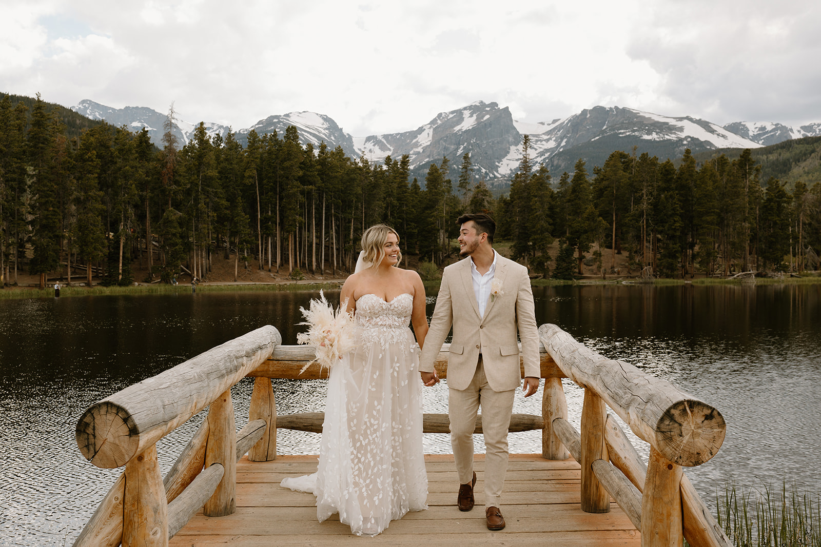 A bride and groom holding hands walking off a dock where they had their wedding ceremony, with the Rocky Mountains behind them.